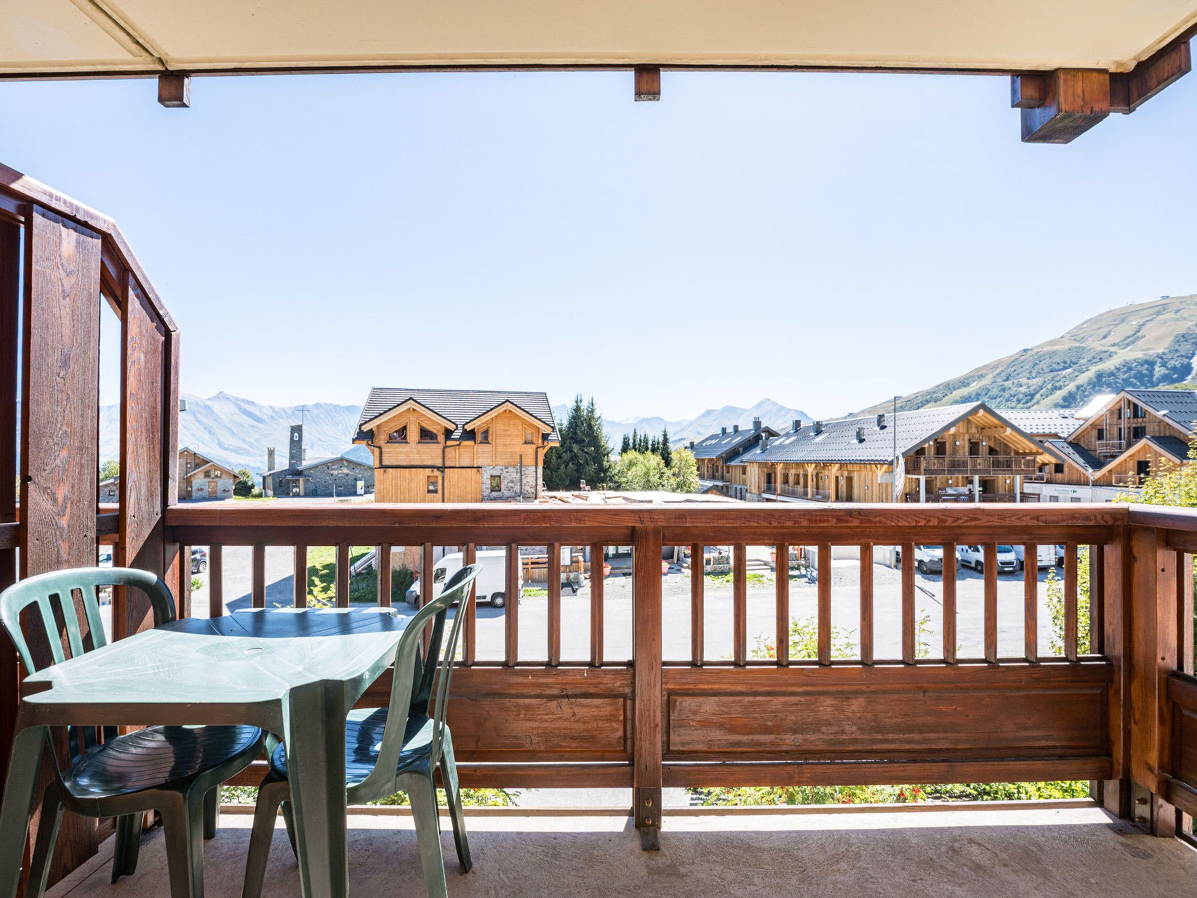 A wooden deck with a table and chairs, overlooking a mountainous landscape with wooden buildings.