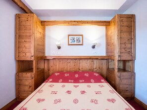 A room with a bed, wooden paneling, two wall-mounted lights, and a framed picture on the wall. - Cozy apartment with balcony - 4 guests (La Toussuire)