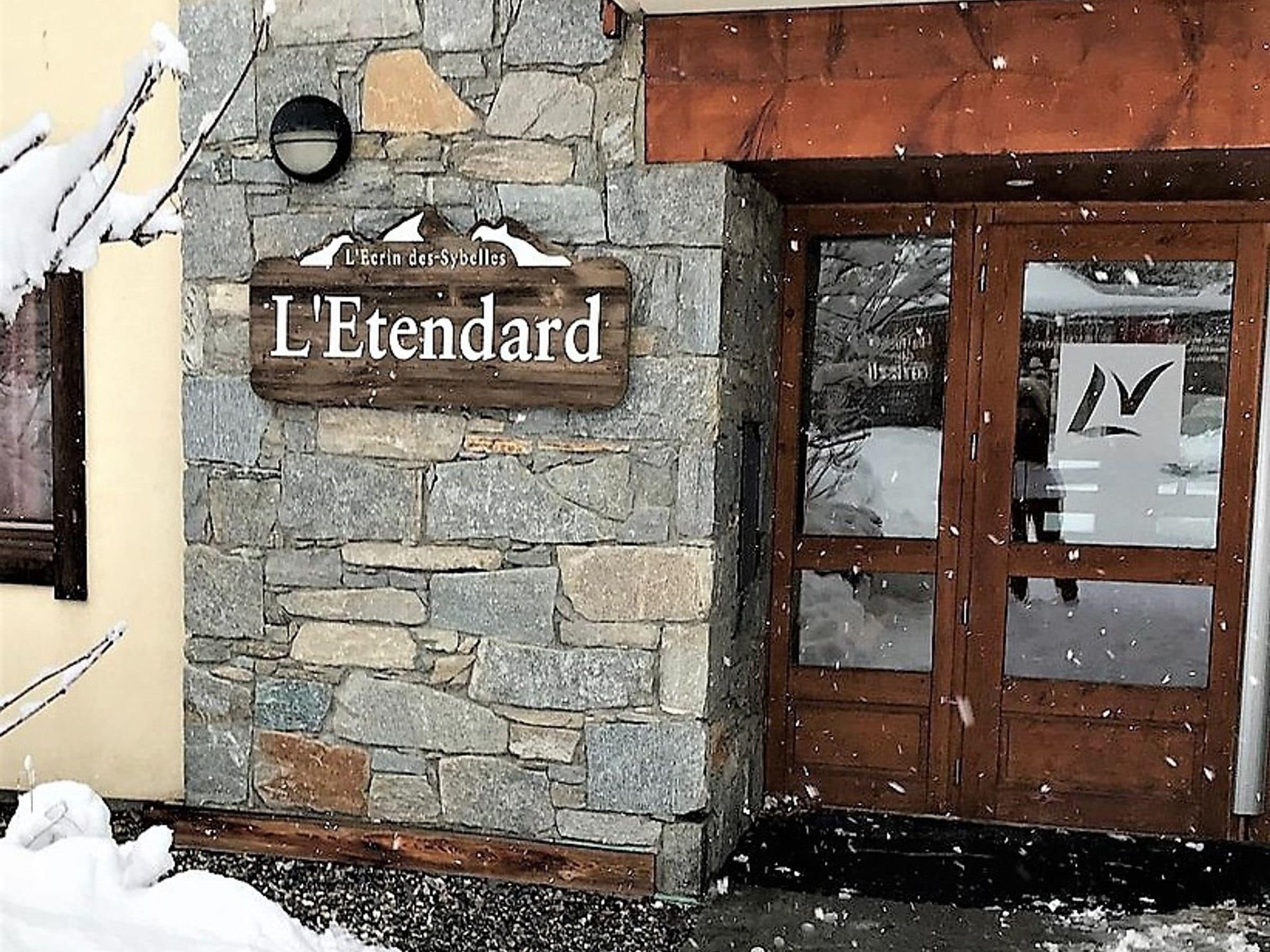 Un bâtiment en pierre avec une enseigne en bois portant l’inscription « L’Etendard » et une porte dotée d’un panneau de verre.