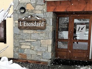 A stone building with a wooden sign reading 'L'Etendard' and a door with a glass panel. - Cozy apartment with balcony - 4 guests (La Toussuire)