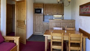A compact kitchen with wooden cabinets, a microwave, and a dining table with chairs. - Cozy apartment with balcony - 4 guests (La Toussuire)
