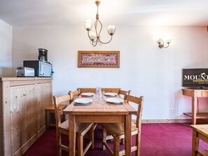 A dining area with a wooden table set for four, a chandelier, and a framed picture on the wall. - Cozy apartment with balcony - 4 guests (La Toussuire)