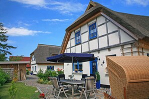 Ein traditionelles Fachwerkhäuschen mit Strohdach, ein Garten mit gepflastertem Weg und Gartenmöbeln.