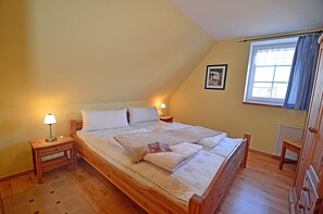 Ein Schlafzimmer mit einem hölzernen Bett, zwei Nachttischen mit Lampen, einem Fenster mit Vorhängen und einer Heizung.