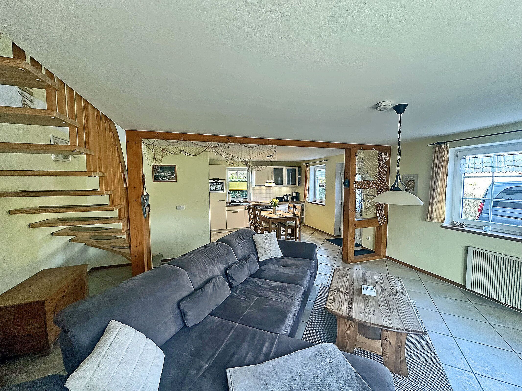 A living room with a sofa, a wooden staircase, a dining area, and a kitchen.