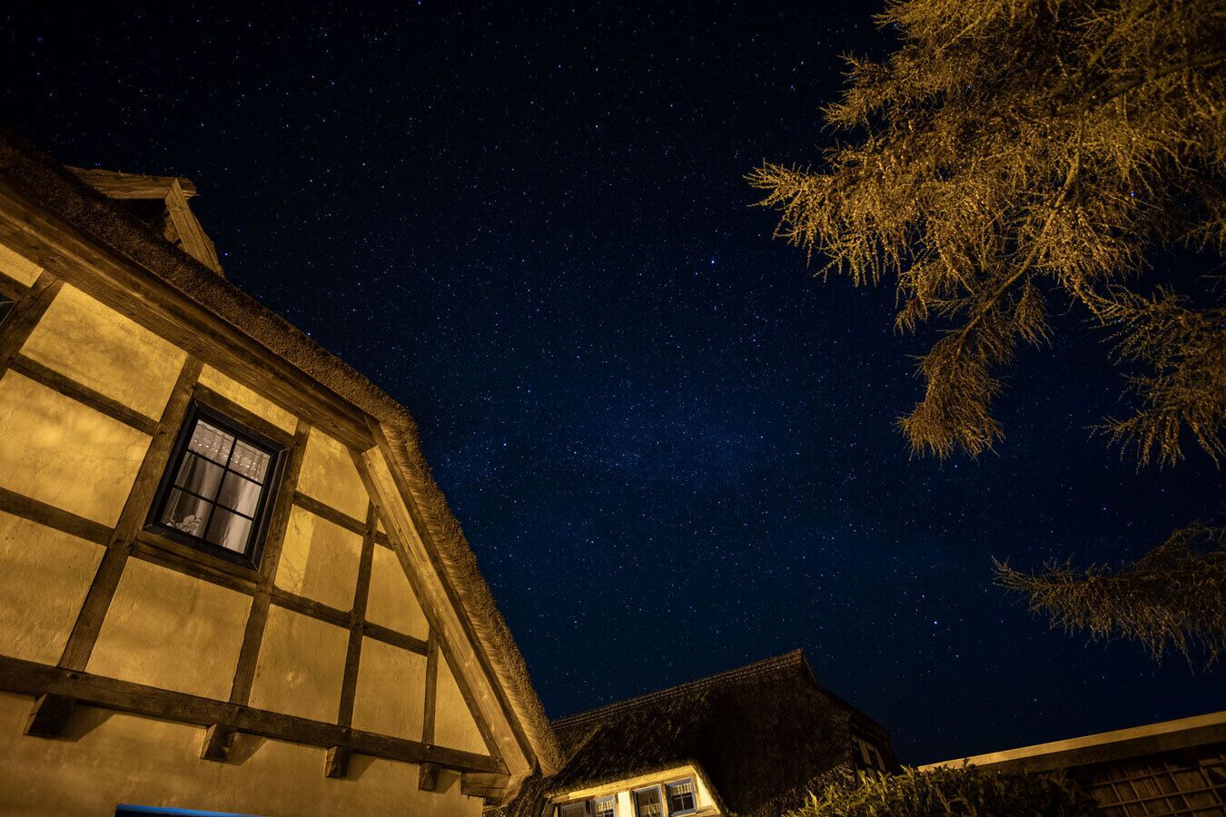 En traditionel bindingsværksbygning med et synligt vindue og en stjerneklar nattehimmel.