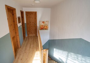Ein schmaler Flur mit Holztüren und einer Treppe, die zu einem Raum mit blauer Wand führt.