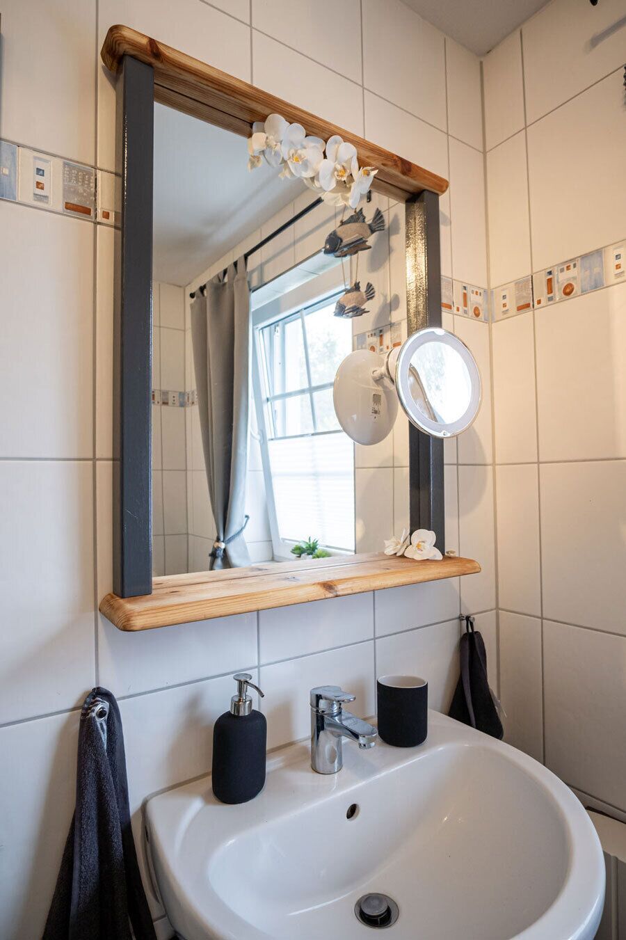 Une salle de bain avec un lavabo blanc, un miroir et une étagère en bois.