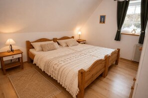Ein Schlafzimmer mit einem Holzbett, zwei Nachttischen mit Lampen, einem Fenster mit Vorhängen und einem Heizkörper.