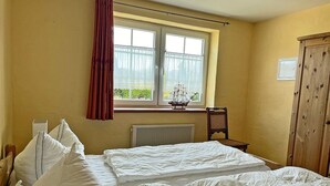 Quarto com duas camas, janela com cortinas, radiador, armário de madeira e uma cadeira.