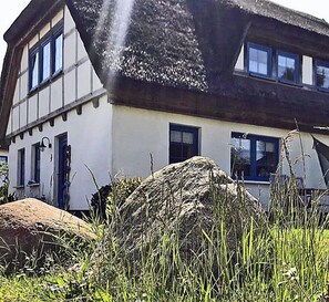 A traditional half-timbered house with a thatched roof, surrounded by grass and a large rock. - 900 meters to the beach, 2 bedrooms, sleeps up to 4, Wi-Fi, pets allowed by arrangement (Breege)