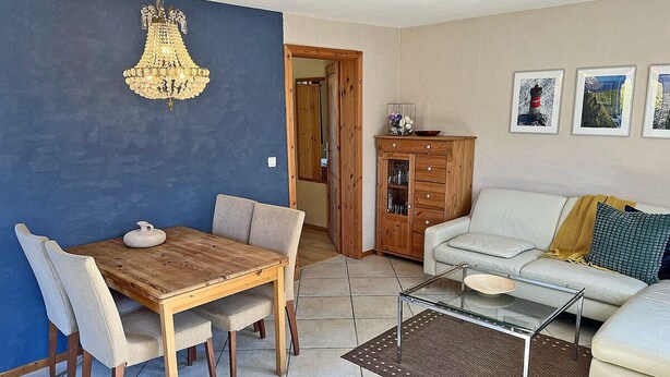 Uma sala de jantar com mesa e cadeiras de madeira, um lustre e um sofá com almofadas.