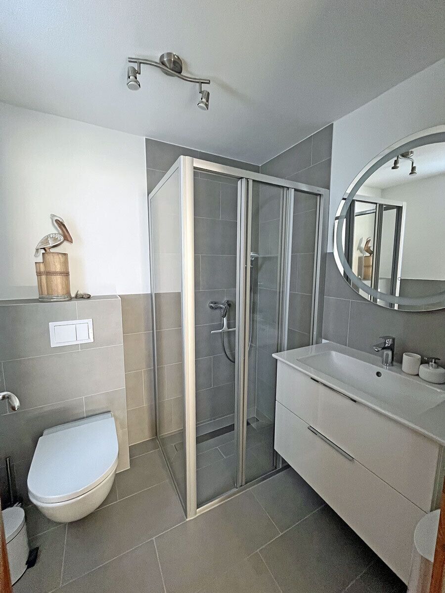 Un bagno moderno con cabina doccia in vetro, un water bianco e un mobile lavabo con specchio.