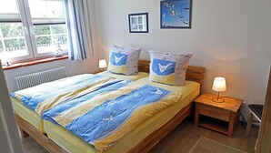 A double bed with a striped bedspread, two pillows with a bird design, a bedside table with a lamp, a framed picture on the wall, and a window with curtains. - 900 meters to the beach, 2 bedrooms, sleeps up to 4, Wi-Fi, pets allowed by arrangement (Breege)