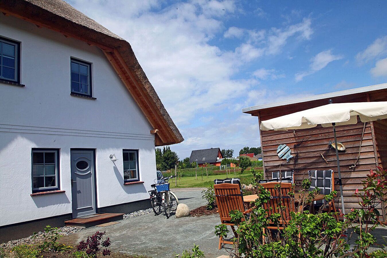 A white building with a thatched roof, a wooden structure with a white awning, and outdoor seating.