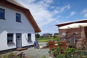 Ein weißes Gebäude mit einem Strohdach, eine Holzkonstruktion mit einer weißen Markise und Außenplätzen.