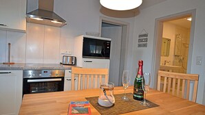 A modern kitchen with a microwave, toaster, and oven. There is a dining table with a book and glasses. - 900 meters to the beach, 2 bedrooms, sleeps up to 4, Wi-Fi, pets allowed by arrangement (Breege)