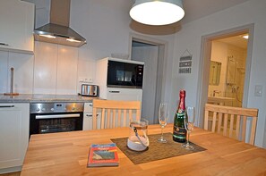 Eine moderne Küche mit Mikrowelle, Toaster und Backofen. Ein Esstisch steht bereit, darauf liegen ein Buch und Gläser.