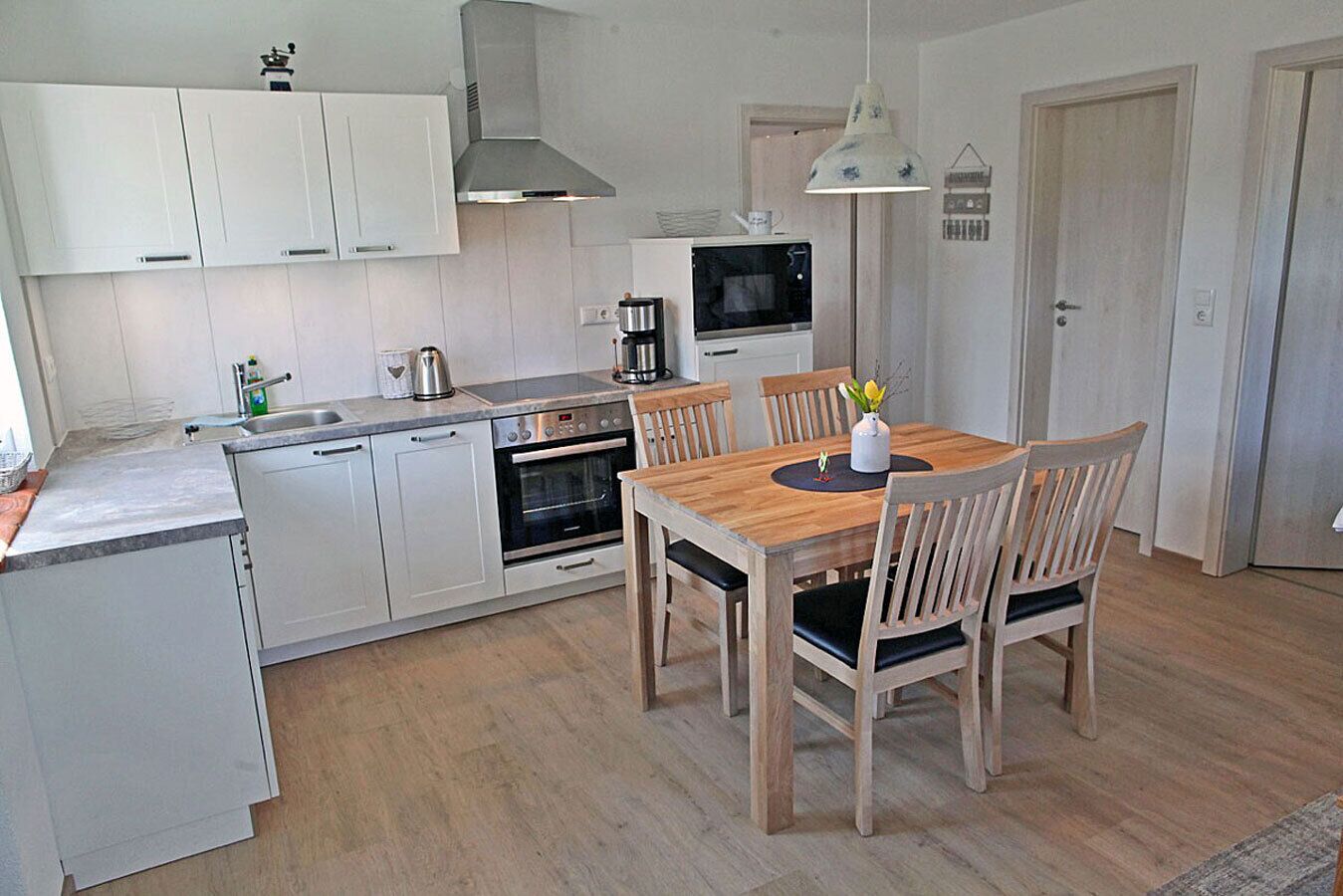 Une cuisine compacte avec des meubles blancs, une table à manger en bois et un four encastré.