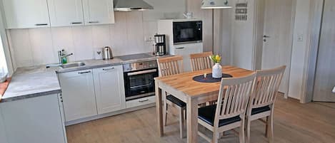 Une cuisine compacte avec des meubles blancs, une table à manger en bois et un four encastré.