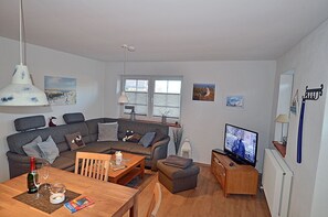 A living room with a sectional sofa, a wooden coffee table, a television, and a dining table with a bottle and glasses. - 900 meters to the beach, 2 bedrooms, sleeps up to 4, Wi-Fi, pets allowed by arrangement (Breege)
