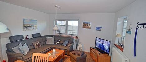 A living room with a sectional sofa, a television, and a wooden coffee table.