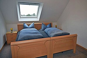 A bedroom with a sloped ceiling, a skylight, a wooden bed with blue bedding, a bedside table with a lamp, and a nightstand with a vase. - About 400 meters from the Baltic Sea beach, with 3 bedrooms, a washing machine, a sauna, and Wi-Fi (Breege)