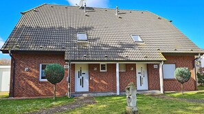 A two-story brick building with a tiled roof, numbered doors, and a small garden with trimmed bushes. - About 400 meters from the Baltic Sea beach, with 3 bedrooms, a washing machine, a sauna, and Wi-Fi (Breege)