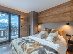 A bedroom with a large bed, wooden walls, a view of mountains, and a balcony. - Bright apartment - 10 guests (Megève)