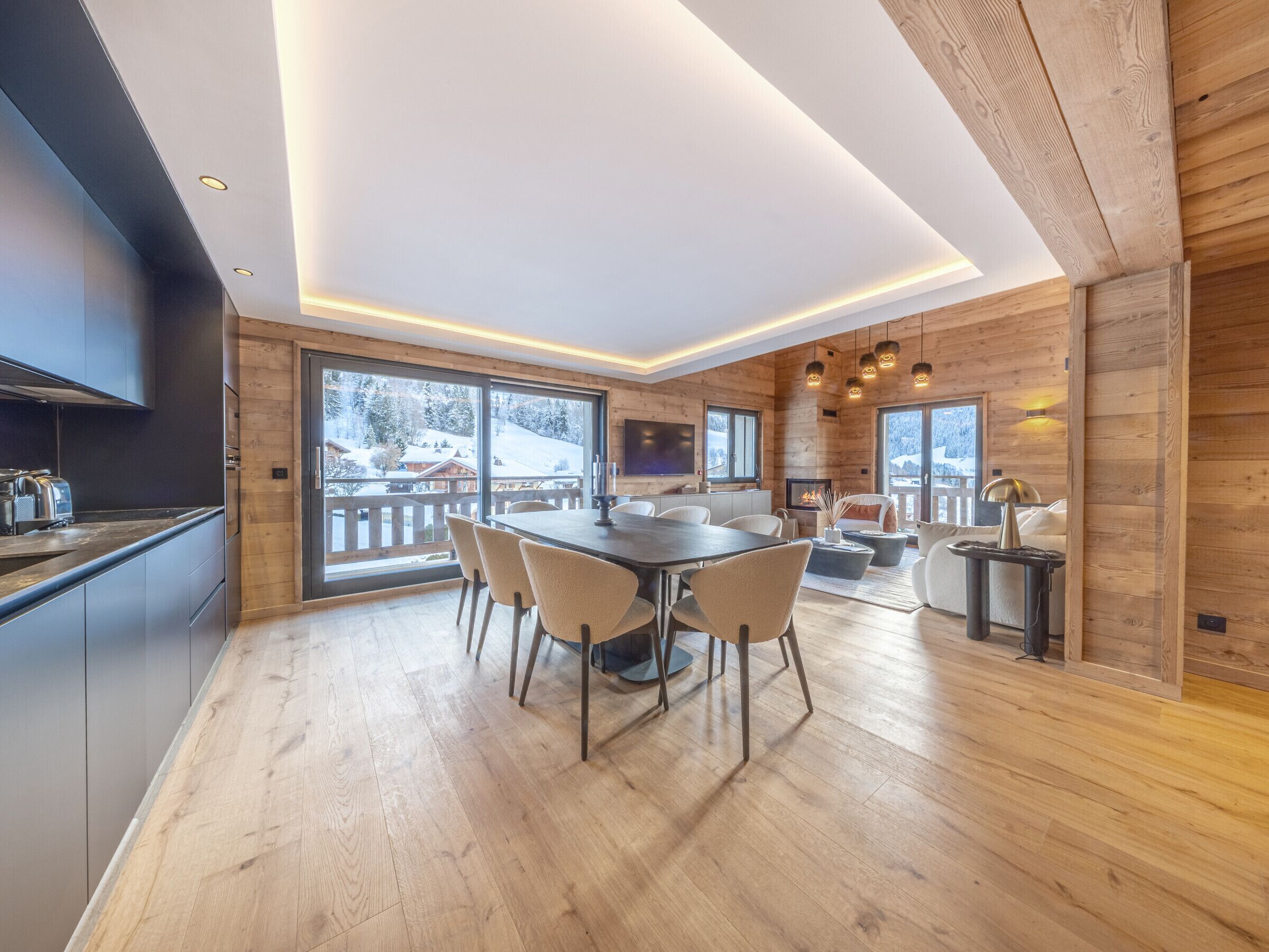 A modern kitchen with a dining area, wooden walls, and large windows overlooking a snowy landscape.