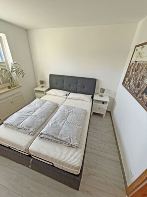 Ein Schlafzimmer mit einem großen Bett, Nachttischen, einem Heizkörper und einem Fenster mit Pflanze.