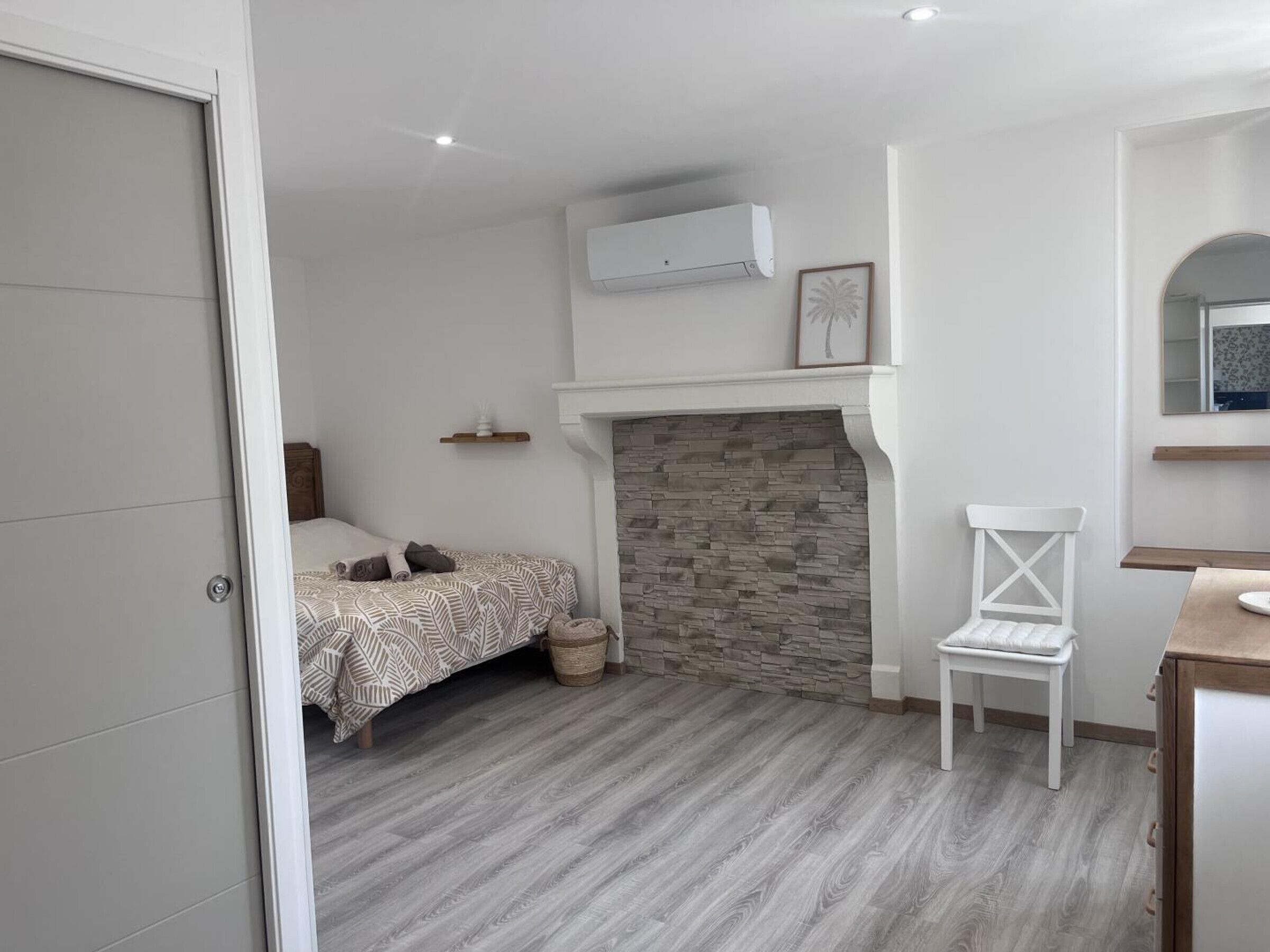 Ein Schlafzimmer mit Bett, einem Sessel, einem Kamin und einem Spiegel.