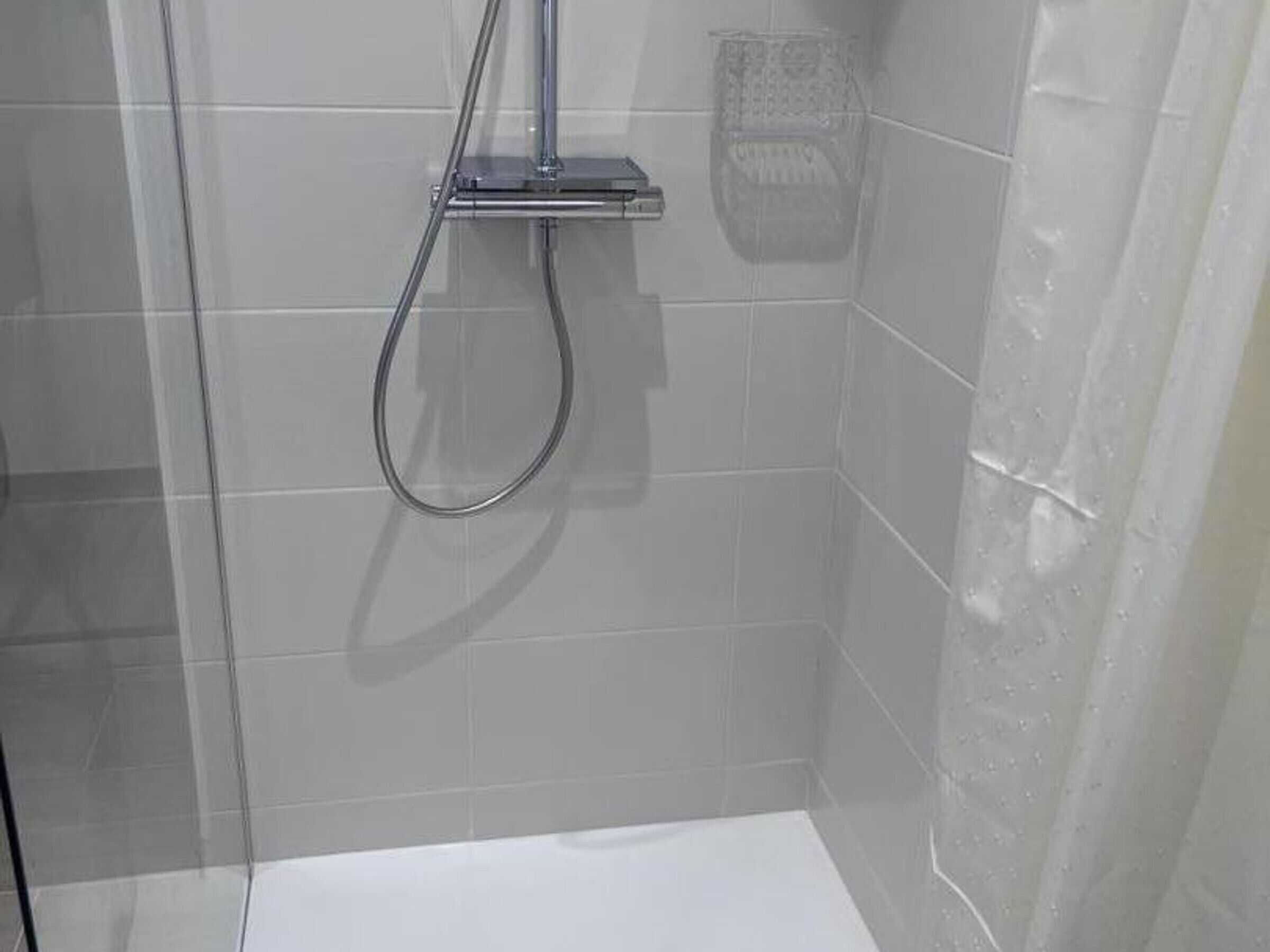 Ein Duschbereich mit Glastür, Brausekopf aus Chrom und weiß gefliesten Wänden.
