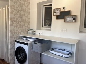 A laundry room with a washing machine, a dryer, and a shelf with baskets and a small plant.