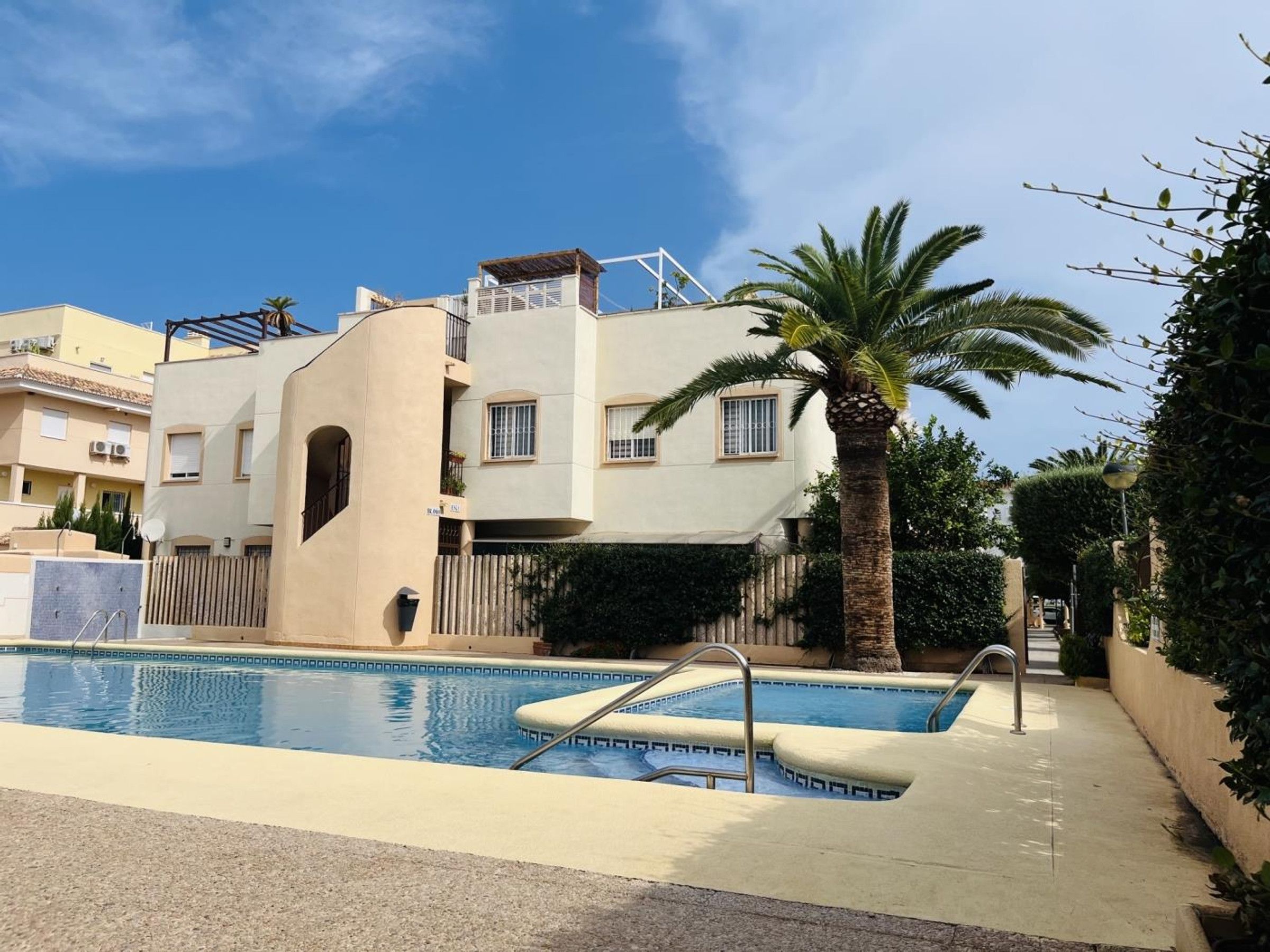 Un edificio residencial con piscina, una palmera y un cielo azul despejado.