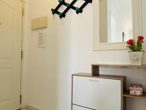 A white door with a brass handle, a wall-mounted black and teal decorative piece, a mirror with a white frame, and a small shelf with a floral vase and a box. - Charming apartment near the sea - 4 guests (Denia)