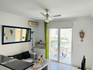Une pièce dotée d’un ventilateur de plafond, d’un grand miroir, d’une table avec un vase et d’une porte-fenêtre coulissante donnant sur un espace extérieur aménagé avec des chaises.