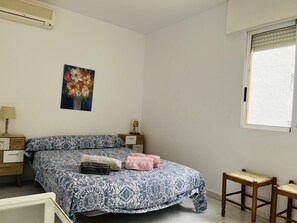 A bedroom with a bed, a nightstand, a lamp, a window, and a painting on the wall. - Charming apartment near the sea - 4 guests (Denia)