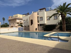 Une piscine dotée d’un espace salon en contrebas, entouré d’un petit muret et d’un chemin pavé.