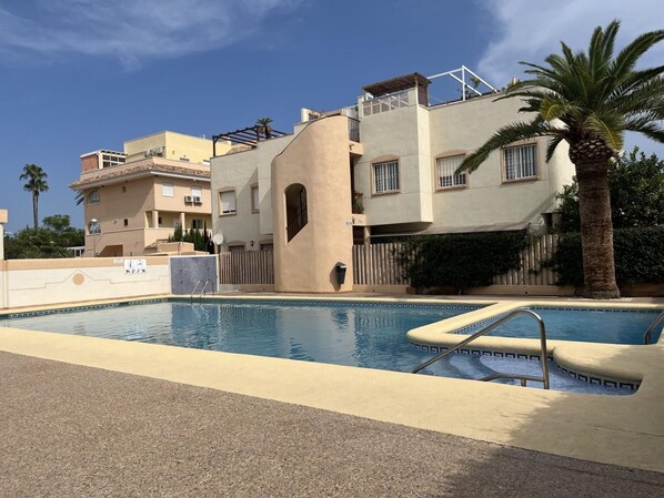 Una piscina con una zona de estar hundida, rodeada por un muro bajo y un camino pavimentado.