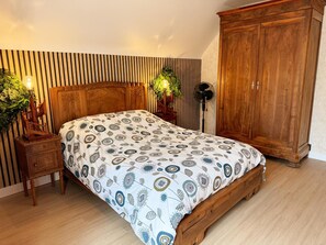 Et soveværelse med en træseng, et natbord med lampe, et garderobeskab og en vægmonteret ventilator.