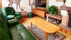 Ein Wohnzimmer mit einem grünen Ledersofa, einem Holztisch, einem Fernseher auf einem Holzständer, einem Kamin mit Ziegelverkleidung und einem gemusterten Teppich.