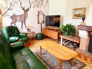 Ein Wohnzimmer mit einem grünen Ledersofa, einem Holztisch, einem Fernseher auf einem Holzständer, einem Kamin mit Ziegelverkleidung und einem gemusterten Teppich.