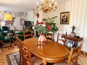 A dining area with a round wooden table, chairs, a chandelier, a television, and a wall-mounted clock. - Charming cottage between nature and culture - 6 guests (Thoury)