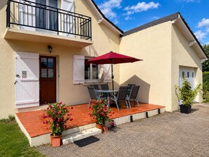En toetagers bygning med en balkon, en rød parasol og en terrasse med bord og stole.