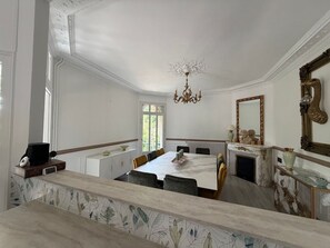 A dining room with a marble table, chairs, a chandelier, and a fireplace.