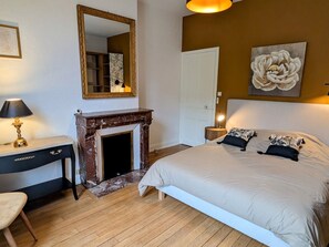 A bedroom with a bed, a desk, a mirror, a fireplace, and a door.