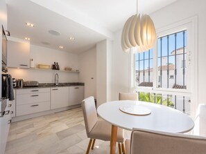 Una cocina moderna con armarios blancos, encimera de mármol y un comedor con mesa redonda y sillas.