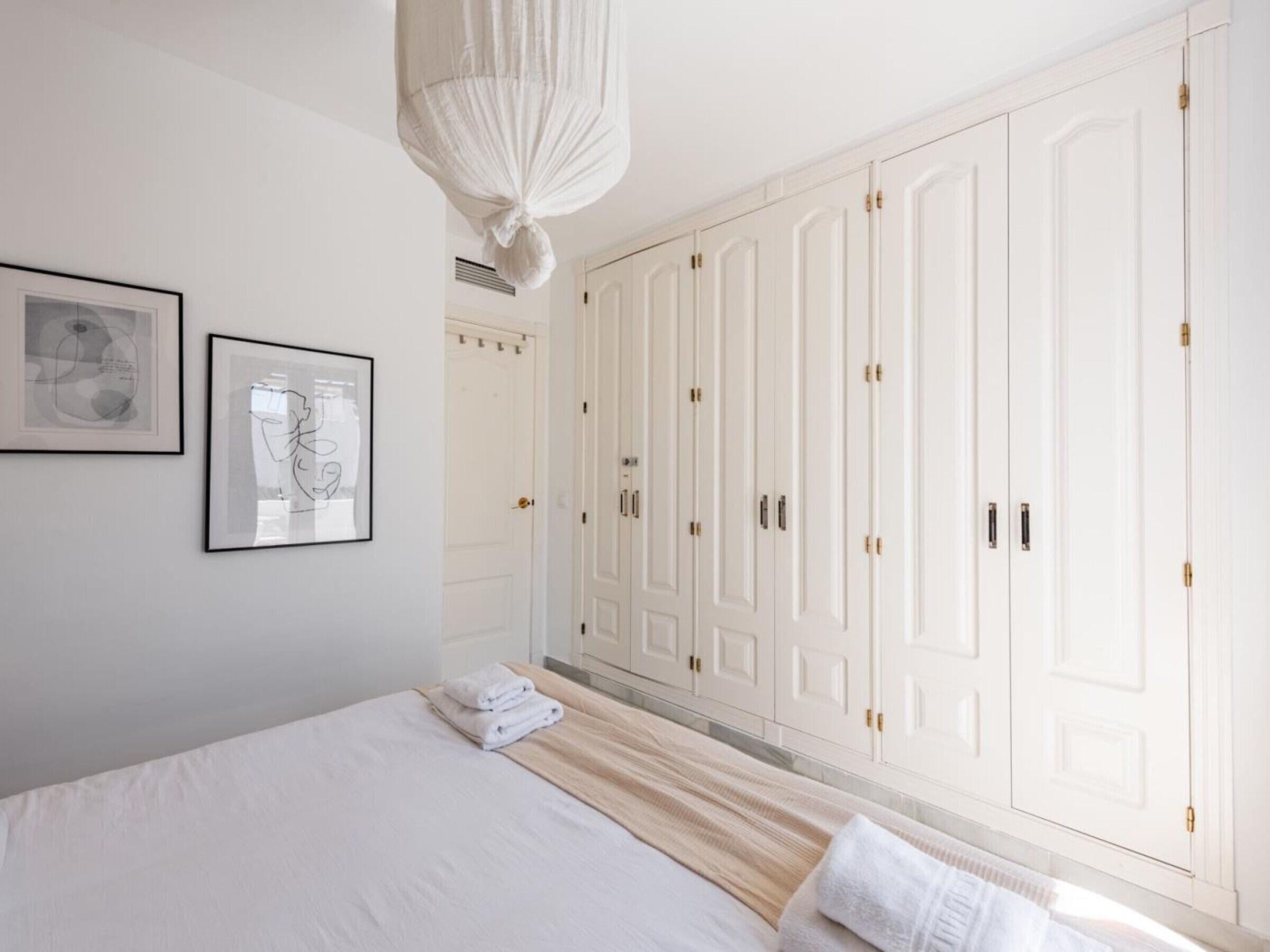 A bedroom with a large bed, a wardrobe, and two framed pictures on the wall.