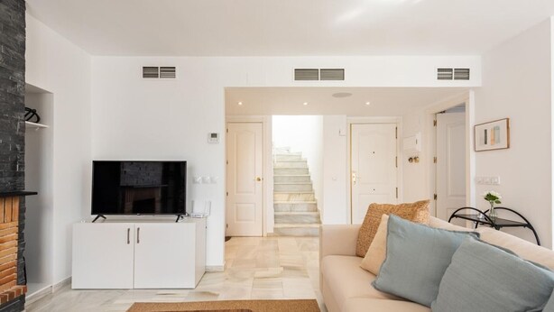 A modern living room with a flat-screen TV, white cabinets, a beige sofa, and a staircase leading to another level. - Modern penthouse with mountain view - 6 guests (Marbella)